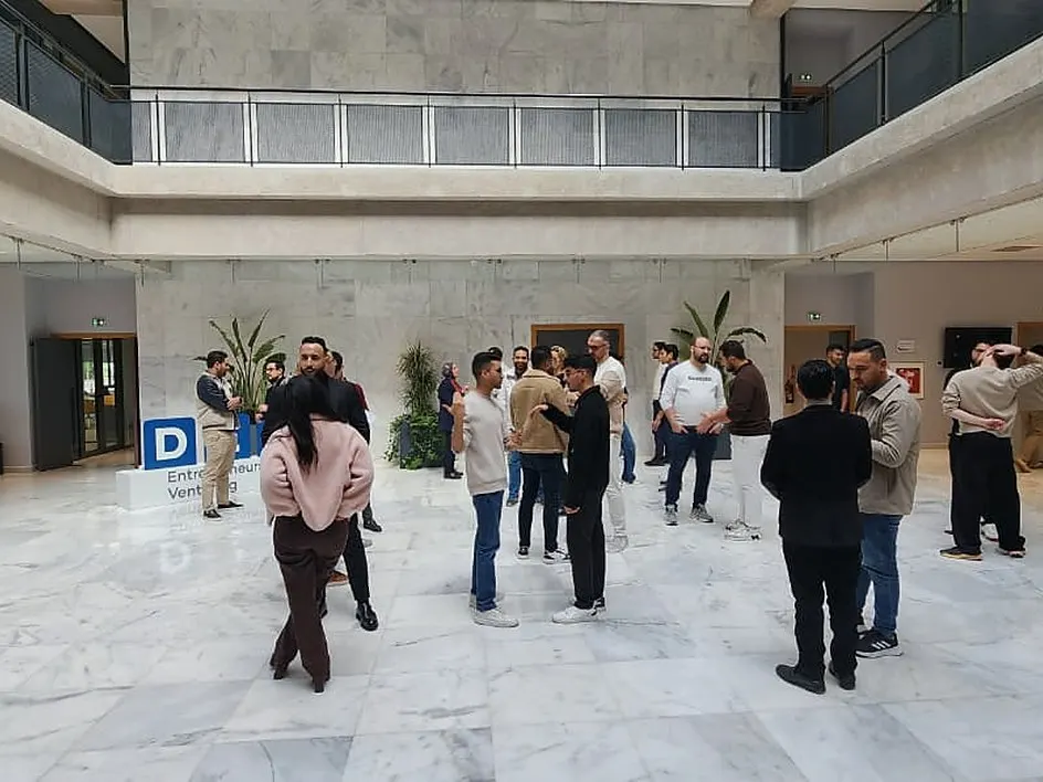 Des participants debout en binômes, dispersés dans un grand hall.