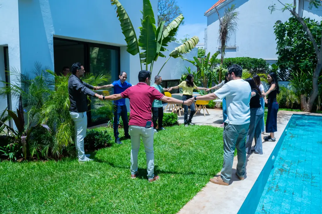 L'équipe en cercle dans le jardin, main dans la main, au bord de la piscine.